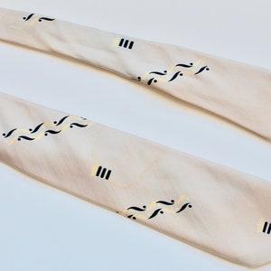 May include: A white silk tie with a black and gold pattern of musical notes and vertical lines.