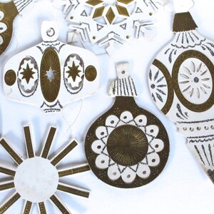 May include: A set of eight vintage paper Christmas ornaments with gold and white designs. The ornaments are shaped like stars, snowflakes, and balls.