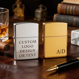Puede incluir: Dos encendedores personalizados, uno plateado y otro dorado, se exhiben sobre una superficie de cuero. El encendedor plateado tiene el texto "CUSTOM LOGO DESIGN OR TEXT". El encendedor dorado tiene las iniciales "AID". Tambi&eacute;n se ven un vaso de whisky, un cigarro y un bol&iacute;grafo.