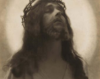 Puede incluir: Retrato en tonos sepia de una persona con cabello largo y barba, usando una corona de espinas. Los ojos de la persona están cerrados, y una suave luz blanca emana de detrás de la cabeza, creando un efecto de halo. La imagen tiene una calidad artística vintage.