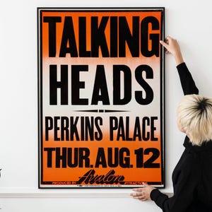 May include: A framed vintage concert poster for Talking Heads at Perkins Palace, with black text on an orange and white background. The poster includes the date, Thursday, August 12, and the Avalon logo.