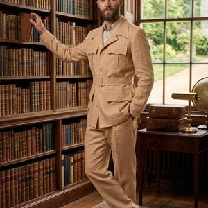 May include: A tan suit with a belted jacket and matching trousers. The suit has multiple pockets and is worn with a light-colored shirt and brown shoes. The setting is a library with bookshelves and a window.