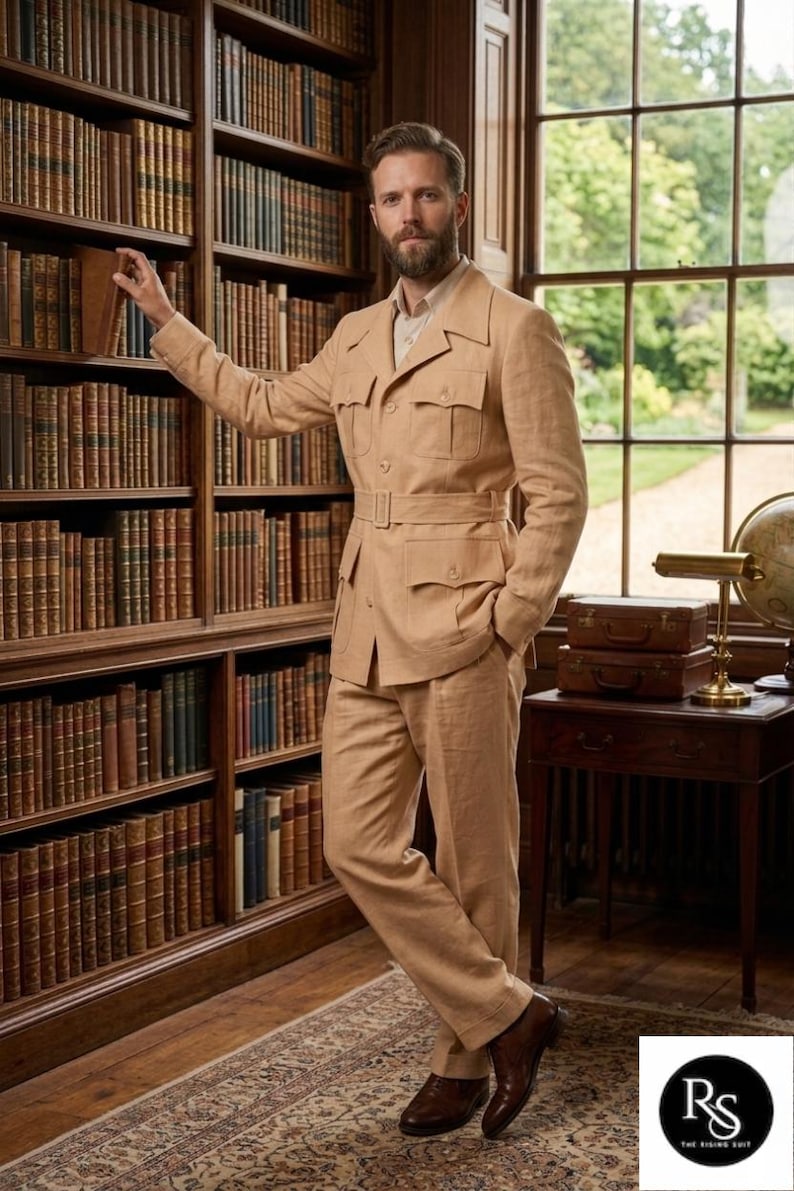 May include: A tan suit with a belted jacket and matching trousers. The suit has multiple pockets and is worn with a light-colored shirt and brown shoes. The setting is a library with bookshelves and a window.