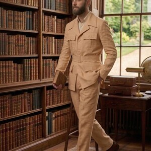 May include: A tan linen suit with a belted jacket and matching trousers. The suit has multiple pockets and is paired with brown leather shoes. The setting is a library with bookshelves and a window.