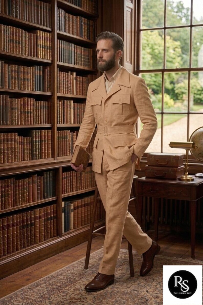 May include: A tan linen suit with a belted jacket and matching trousers. The suit has multiple pockets and is paired with brown leather shoes. The setting is a library with bookshelves and a window.