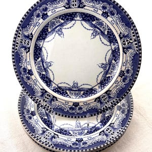 May include: A stack of white ceramic plates with a blue floral design. The plates have a detailed border and a central design. The plates are stacked on top of each other, showcasing the intricate patterns.