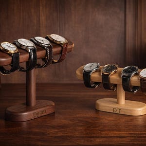 Peut inclure: Deux présentoirs à montres en bois présentant plusieurs montres-bracelets. L'un est brun foncé et contient cinq montres, l'autre est brun clair et contient quatre montres. Les présentoirs sont personnalisés avec des noms.