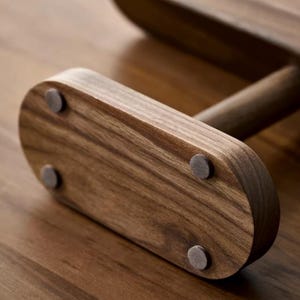 May include: Close-up of a wooden object with a curved, rectangular base. The wood grain is visible, and small, round, gray pads are attached to the bottom. The object has a smooth, polished finish and appears to be part of a larger structure.