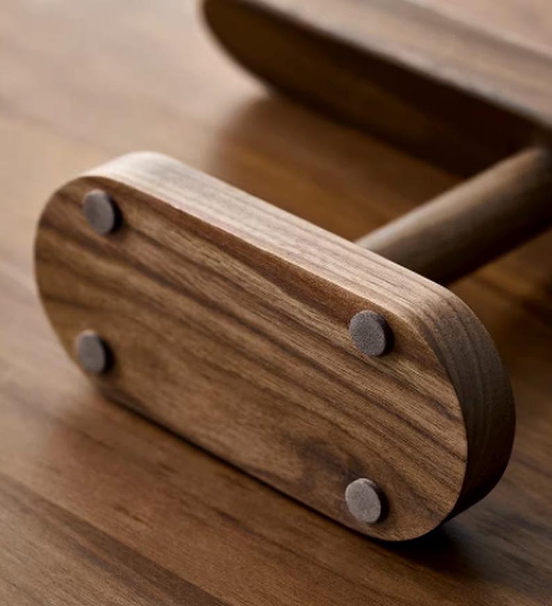 May include: Close-up of a wooden object with a curved, rectangular base. The wood grain is visible, and small, round, gray pads are attached to the bottom. The object has a smooth, polished finish and appears to be part of a larger structure.