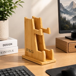 May include: A light brown bamboo stand with a vertical design featuring two tiered horizontal supports for holding items. The base is rectangular and the side of the stand is clearly marked with the black printed letters P&G in a sans-serif font.