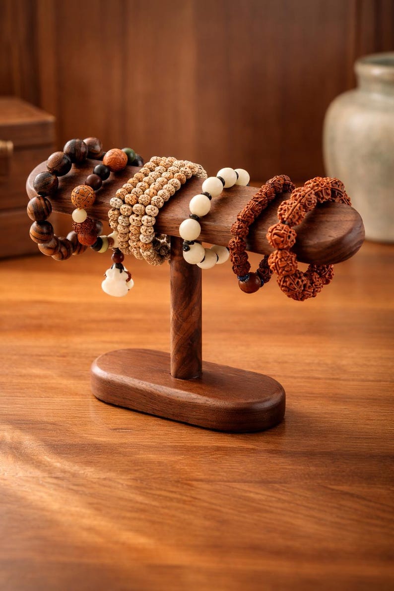 May include: A wooden bracelet display stand holding several beaded bracelets. The bracelets are various colors and textures, including brown, beige, and white. The stand is made of dark wood and has a simple, elegant design.