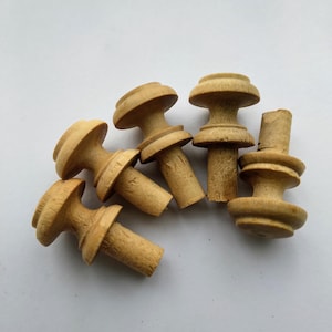 May include: Six wooden knobs with a rounded top and a cylindrical base. The knobs are a light brown colour and have a smooth finish.