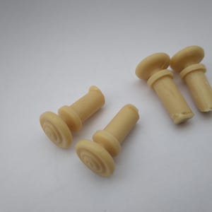 Peut inclure: Cinq embouts de pieds de meubles en plastique beige avec un dessus rond et une base cylindrique.