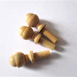 May include: Three unfinished wooden furniture plugs are shown. Each plug has a rounded, decorative top and a cylindrical peg. The plugs are light brown and appear to be made of natural wood.