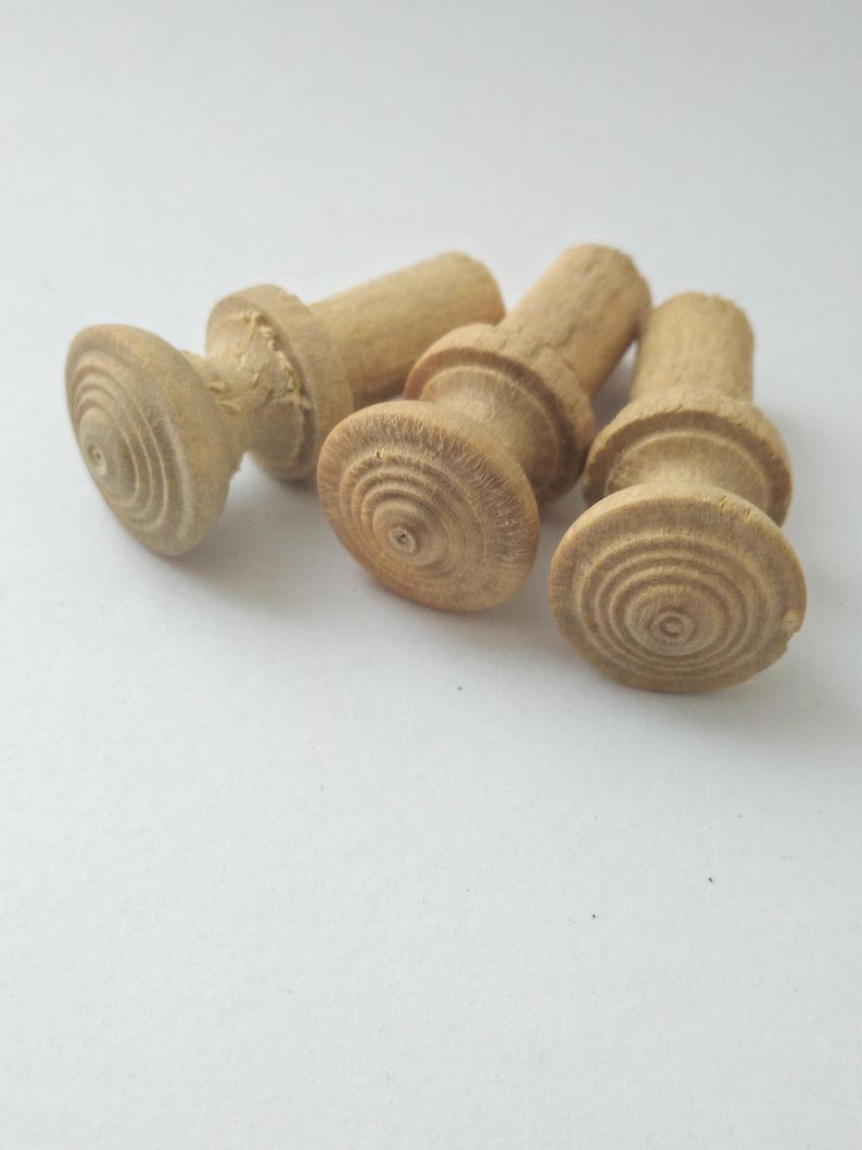 May include: Four unfinished wooden knobs with a light brown color. Each knob has a rounded, grooved base and a cylindrical top. The knobs are arranged on a white surface.