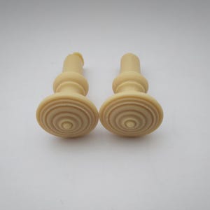 May include: Two ivory-coloured plastic knobs with a circular, ridged design. The knobs have a small, raised centre point.
