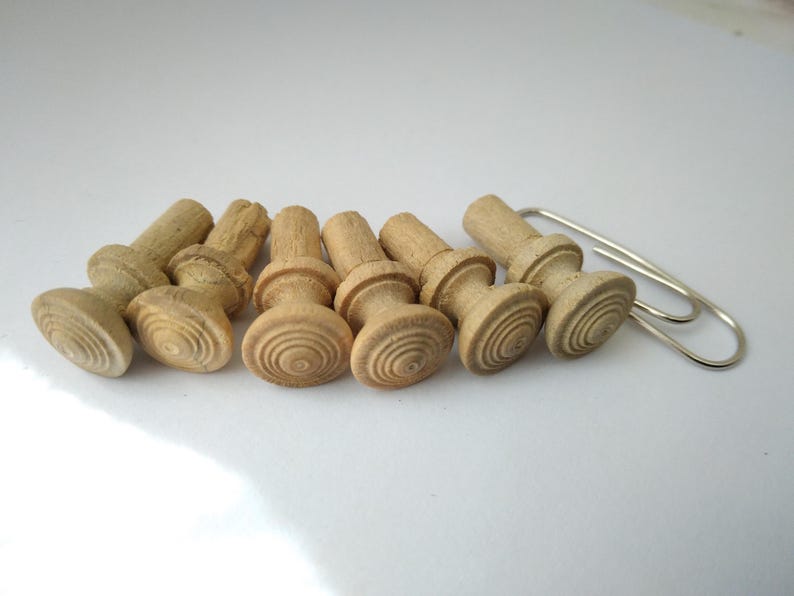 May include: A collection of seven unfinished wooden knobs with a decorative, layered design. The knobs are light brown and arranged in a row, with a silver paperclip next to them. These are likely for a craft or furniture project.