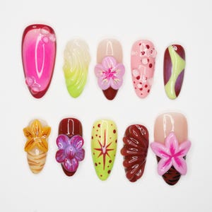 Peut inclure: Collection de dix faux ongles aux designs variés. Les ongles présentent des couleurs vives comme le rose, le jaune, le rouge et le vert, avec des éléments décoratifs tels que des fleurs, des bulles et des motifs abstraits. Présentés sur fond blanc.
