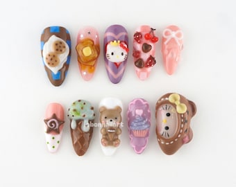 Puede incluir: Diez diseños de uñas con varios motivos. Los diseños incluyen una galleta, tostadas, Hello Kitty, cerezas, un lazo, una estrella, helado, un oso, una magdalena y un reloj. Las uñas están pintadas en marrón, rosa, morado y blanco.
