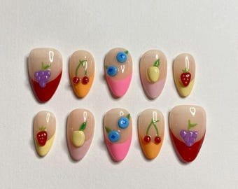 May include: A set of ten artificial nails with a nude base, each adorned with a different fruit design. The fruits include grapes, cherries, blueberries, apples, and strawberries, with colorful accents on the tips.
