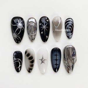 Könnte beinhalten: Ein Set aus zehn mandelförmigen Kunstnägeln mit verschiedenen Designs. Die Nägel weisen eine Mischung aus Schwarz, Silber und Weiß auf. Designs umfassen Spinnennetz-, Wirbel-, Stern- und geometrische Muster. Der Text "ObonNailArt" ist auf einem Nagel sichtbar.