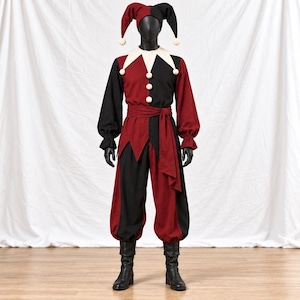 May include: A jester costume featuring a two-toned red and black long-sleeved tunic with a white pointed collar, matching loose trousers, a waist sash, and a three-pointed jester hat. The outfit is accented with small white pom-poms.