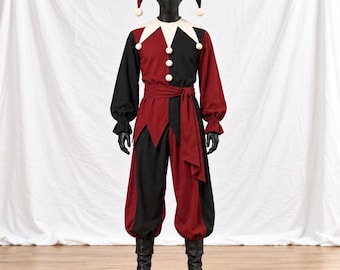 May include: A jester costume featuring a two-toned red and black long-sleeved tunic with a white pointed collar, matching loose trousers, a waist sash, and a three-pointed jester hat. The outfit is accented with small white pom-poms.