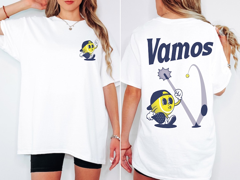 May include: White t-shirt with a cartoon illustration of a yellow tennis ball character wearing a hat and holding a racket on the front. The back of the shirt has the word "Vamos" in blue text and a cartoon illustration of a tennis ball character hitting a ball with a racket.