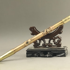 May include: A vintage brass pipe with a dragon design, resting on a dark wooden stand. The pipe has a long, slender body with a bowl at one end and a mouthpiece at the other. The dragon is intricately carved.