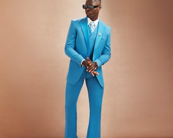 May include: A stylish turquoise suit with a matching vest and flared pants. The suit features a white dress shirt and a light blue patterned tie. The person is wearing black sunglasses and black dress shoes. A small pin is on the suit's lapel.