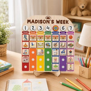 May include: A wooden weekly activity calendar titled MADISON'S WEEK with seven vertical columns in rainbow colors. Each column features numbered circular markers and square wooden tiles with colorful illustrations of daily tasks like school, sports, and chores.