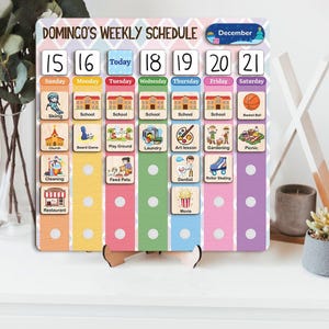 May include: A rectangular weekly schedule board titled Domingo's Weekly Schedule with a December label. It features columns for days of the week, numbered date tiles, and various activity icons including school, sports, and chores on a colorful background.