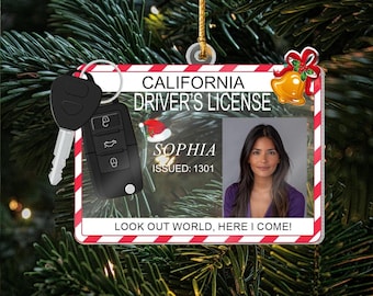May include: A Christmas ornament shaped like a California driver's license with a photo of a woman named Sophia. The ornament includes a car key and the text "LOOK OUT WORLD, HERE I COME!" against a backdrop of a Christmas tree.