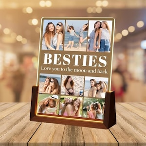May include: A wooden-framed photo display with the word "BESTIES" in large white letters. The display features multiple photos of friends and the phrase "Love you to the moon and back". The display is on a wooden table.