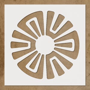 May include: A white stencil with a circular design. The design features a central circle surrounded by curved, geometric shapes radiating outwards. The stencil is on a brown background.