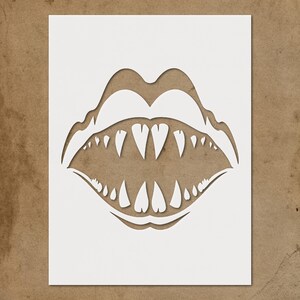 May include: A white stencil cut-out of a mouth with sharp, heart-shaped teeth. The design features a wide open mouth with detailed upper and lower lips, creating a bold and edgy aesthetic. The stencil is on a brown background.
