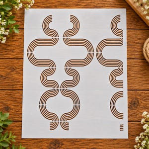 May include: A white rectangular stencil sheet featuring a repeating pattern of brown, multi-line, wavy, and curved geometric shapes. The design consists of interconnected, flowing lines that create a series of symmetrical, abstract, and rhythmic forms.