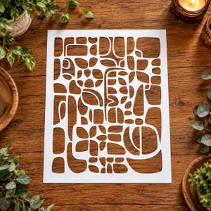 May include: A rectangular white stencil sheet featuring a complex, laser-cut pattern of various organic, rounded, and geometric shapes. The design consists of interconnected negative spaces that form a dense, abstract mosaic of irregular forms.