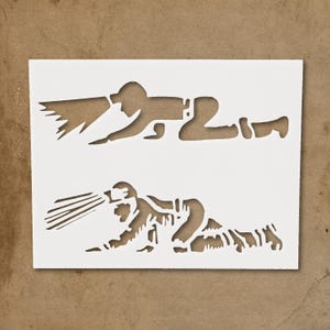 May include: A white stencil featuring two firefighter figures in action. Each figure is depicted in a crawling position, with one spraying water and the other emitting a stream of flames. The stencil is on a brown background.