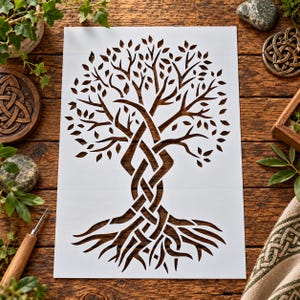 May include: A white rectangular stencil featuring a detailed cutout design of a tree with an intricate, interwoven trunk and root system. The branches extend outward with numerous leaf-shaped cutouts, creating a symmetrical, artistic pattern.