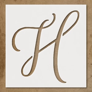 May include: A white stencil with a cutout of the cursive letter "H" in a brown color. The stencil is on a brown background. The letter has a flowing, elegant design, suitable for crafts and decor.