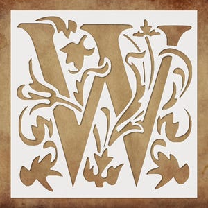 May include: A white stencil featuring the letter "W" in an ornate, stylized font, surrounded by floral and leaf designs. The stencil is set against a brown, textured background, creating a contrast in color and texture.