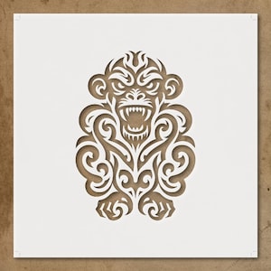 May include: A brown paper cut-out of a stylized monkey with an open mouth and sharp teeth. The monkey has an angry expression and is surrounded by swirling, tribal-style patterns. The artwork is set against a white background.