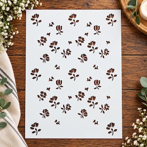 May include: A rectangular white stencil sheet featuring a repeating pattern of die-cut flowers and small heart shapes. The design consists of multiple individual floral motifs arranged in a scattered layout across the entire surface of the sheet.