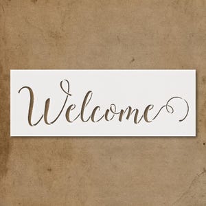 May include: A white stencil with the word "Welcome" cut out in a cursive font. The stencil is rectangular and sits against a brown background.