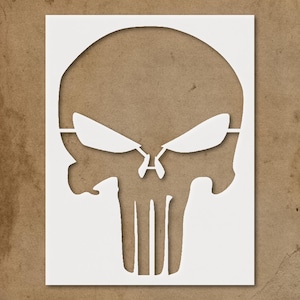May include: White stencil of a skull with eye and nose details, set against a brown background. The skull design features a prominent brow line and vertical lines representing teeth. The stencil is cut from a white material.