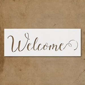 May include: A white stencil with the word "Welcome" cut out in a cursive font. The stencil is rectangular and sits against a brown background.