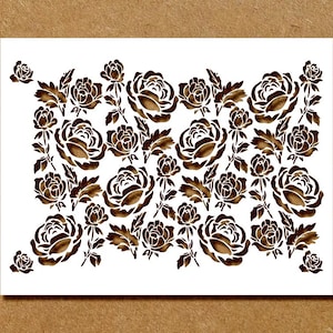 May include: A white rectangular stencil featuring a repeating pattern of brown roses and leaves. The floral design is evenly spaced across the stencil, creating a decorative border. The stencil is ideal for crafts and DIY projects.