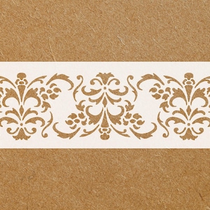 May include: A stencil featuring a repeating ornamental design in a warm, golden-brown color. The pattern includes floral and scroll elements, creating a symmetrical border on a white rectangular background.