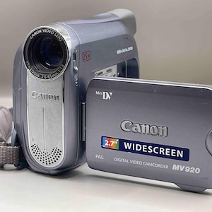 Peut inclure: Caméscope numérique Canon MV920 argenté avec écran large de 2,7 pouces. Le caméscope dispose d'un objectif vidéo Canon avec zoom 25x et d'un port Mini DV. Il y a une dragonne grise.